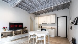 Un salon moderne doté d’un téléviseur à écran plat, d’une table à manger avec des chaises, d’un plancher en bois et d’un coin cuisine avec des placards et une cuisinière.