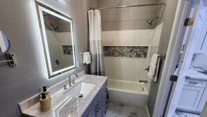 A modern bathroom with a large mirror, a sink, and a shower area.
