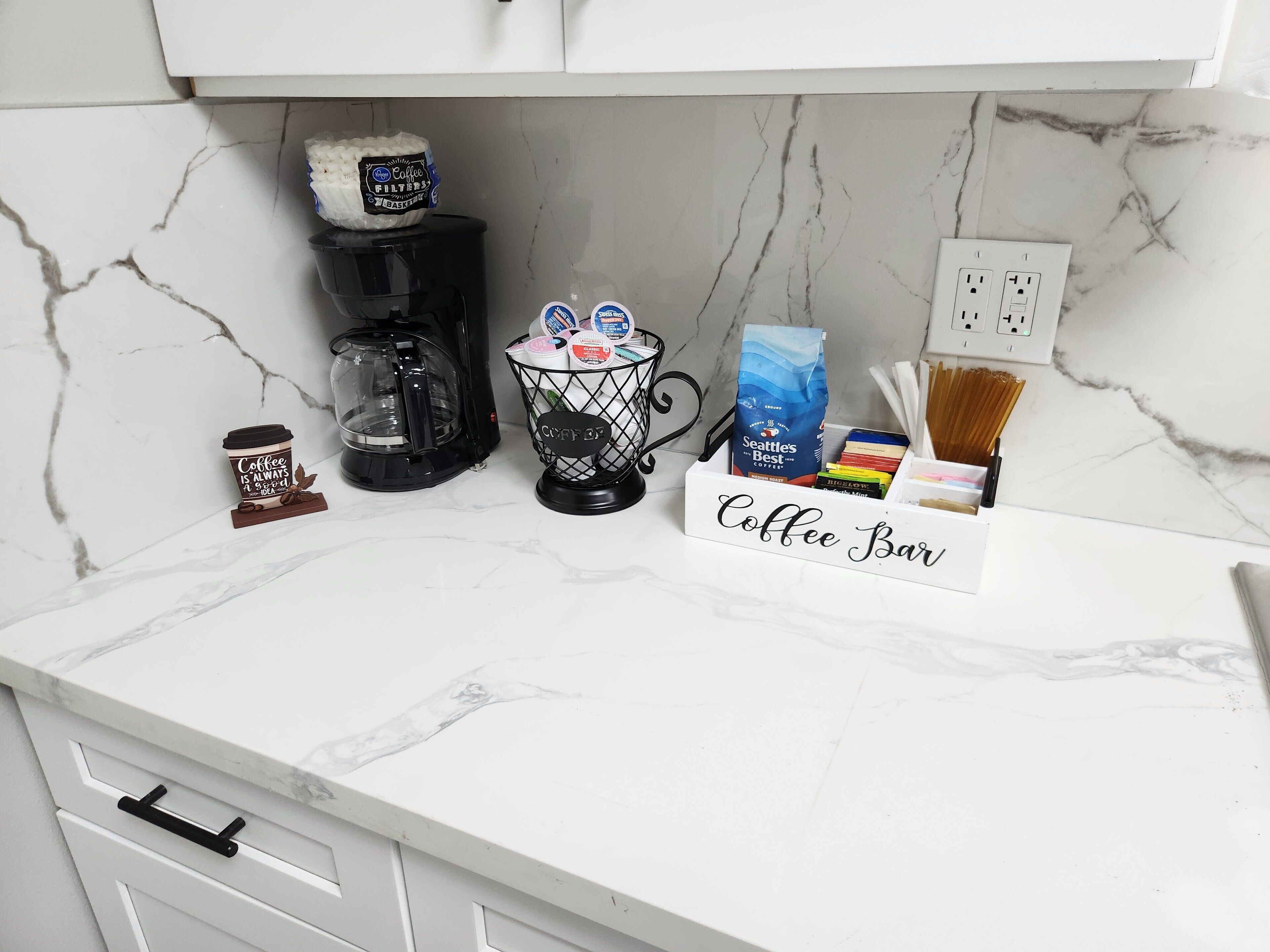 A kitchen counter with a coffee maker, a coffee cup, a coffee filter basket, and a coffee bar sign.