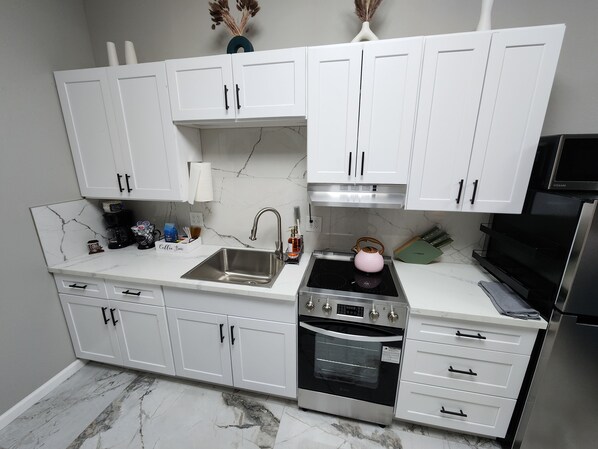Een moderne keuken met witte kasten, een roestvrijstalen spoelbak, een ingebouwde oven en een magnetron.