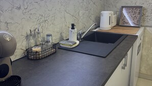 Une cuisine moderne avec un dosseret en marbre, un évier encastré, une machine à café et une bouilloire posées sur le plan de travail.
