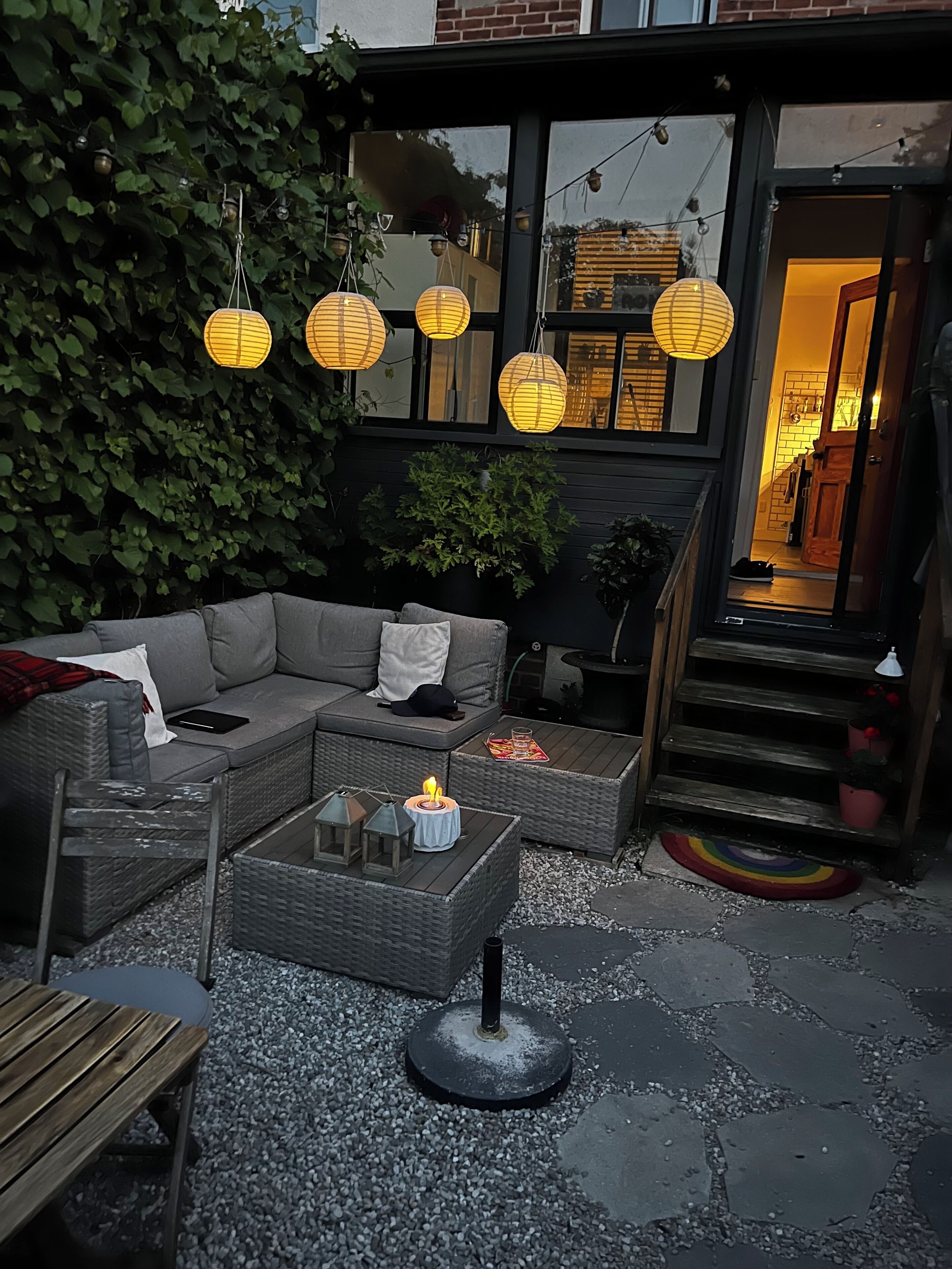 An outdoor seating area with a sofa, coffee table, and chairs, surrounded by greenery and decorative lanterns.