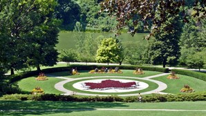 A well-manicured garden with a central circular flower bed, surrounded by neatly trimmed hedges and trees. - Trendy Roncesvalles Village. Just steps to shopping, dining, Lake Ontario (Toronto)
