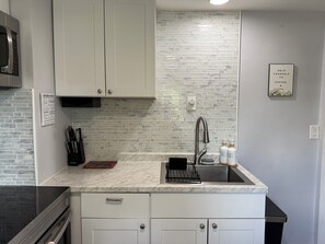 A modern kitchen with white cabinets, a marble countertop, a stainless steel sink, and a microwave.
