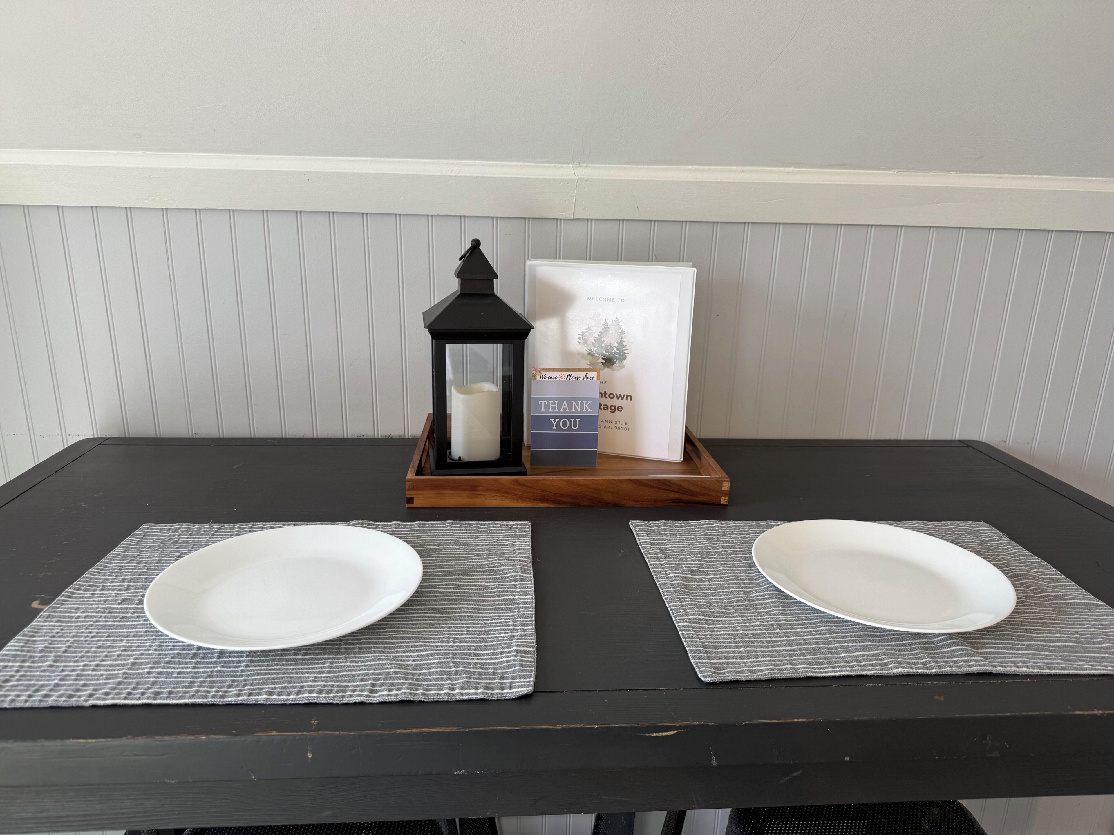 A table with two white plates on placemats, a black lantern, and a welcome sign.