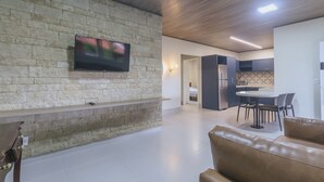 Een moderne woonkamer met een stenen muur, een flatscreen televisie, een leren bank en een eetgedeelte met een ronde tafel en stoelen.
