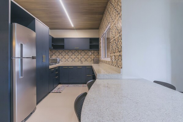 A modern kitchen with dark cabinets, a stainless steel refrigerator, a granite countertop, and patterned backsplash tiles.