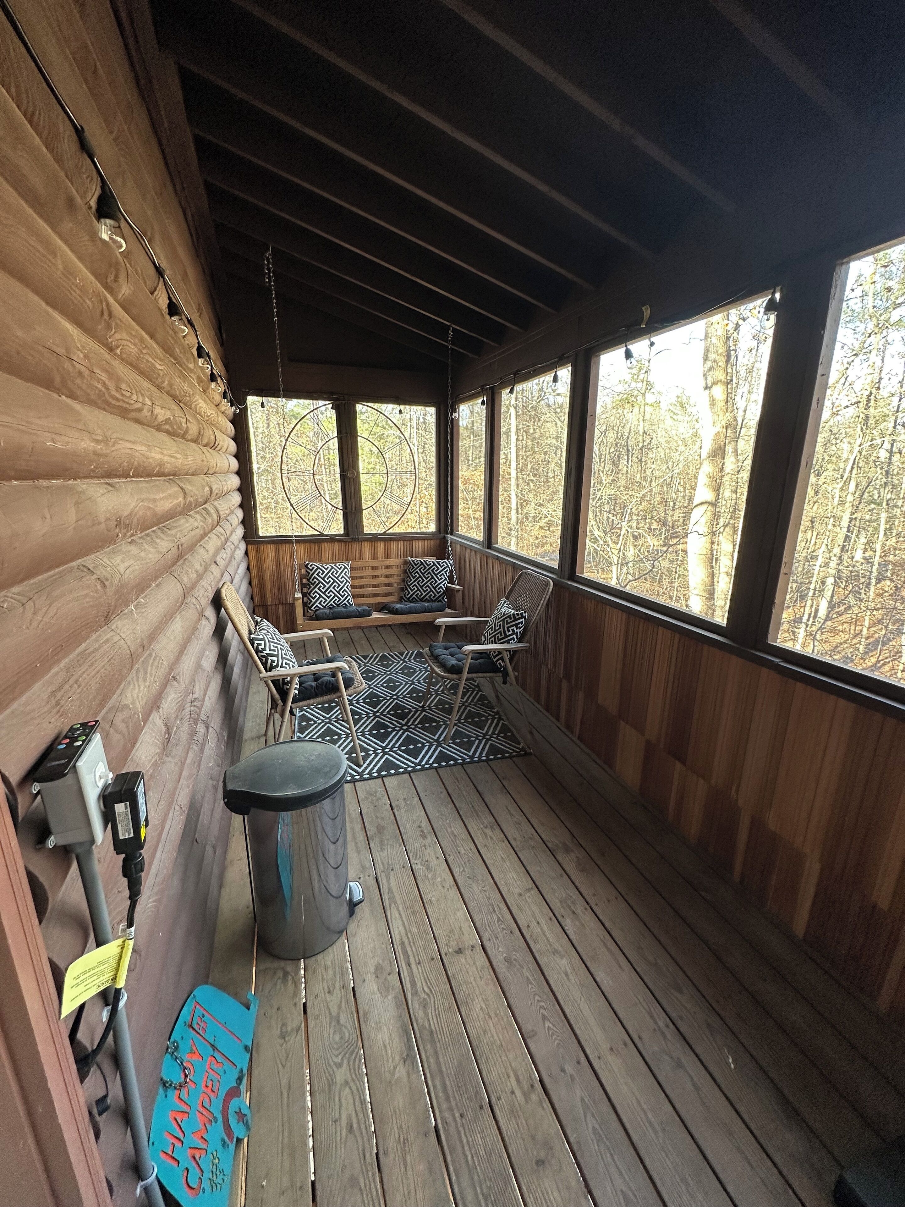 Eine Holzterrasse mit Sitzgelegenheit, einem Mülleimer und einem Schild mit der Aufschrift 'Happy Camper'.
