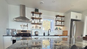 A modern kitchen with a large island, stainless steel appliances, and wooden shelves.