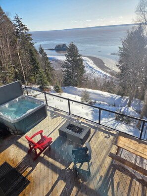 Eine Holzterrasse mit Whirlpool, Feuerstelle und Außenmöbeln.