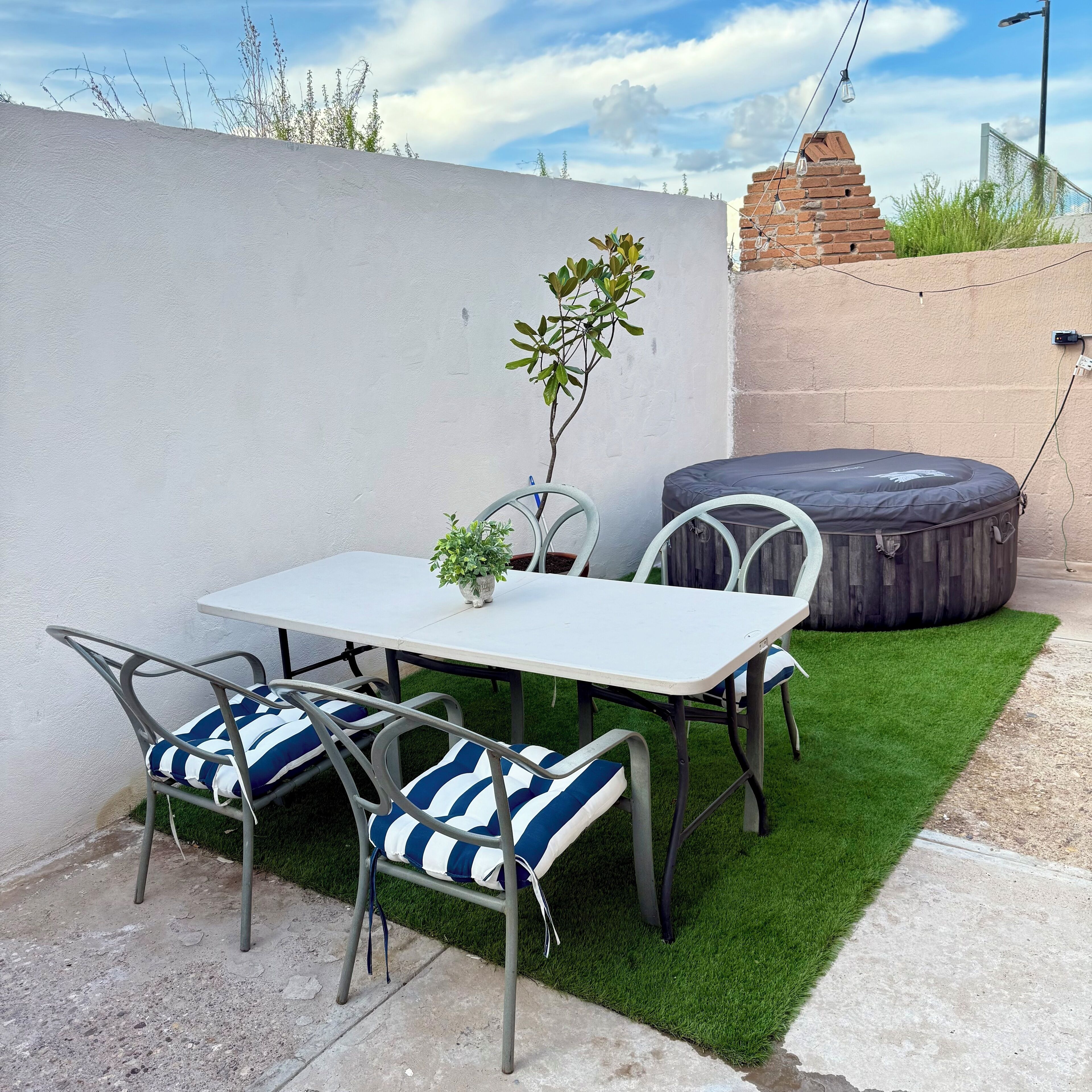 Un patio con una mesa, sillas, una planta pequeña en maceta y un reposapiés de madera.