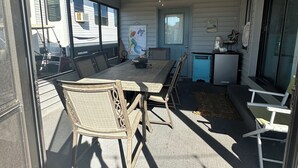 A covered outdoor seating area with a table and chairs, a ceiling fan, and a view of a trailer through the window. - Kelley's Beach Hut "Venture Out" lot 241 (Panama City)