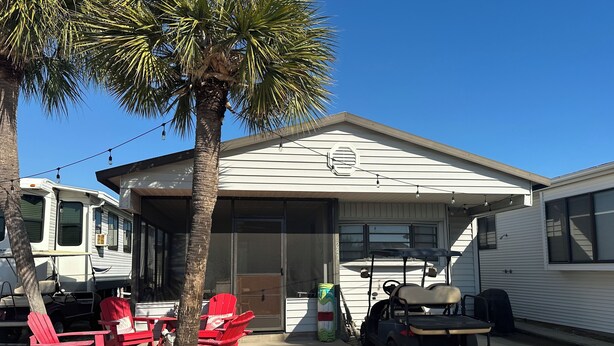 A mobile home with a covered porch, red Adirondack chairs, a golf cart, and a palm tree. - Kelley's Beach Hut "Venture Out" lot 241 (Panama City)