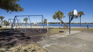 A park with swings and a basketball hoop by a waterfront. - Kelley's Beach Hut "Venture Out" lot 241 (Panama City)