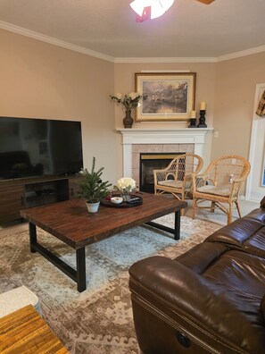 Una sala de estar con televisor, chimenea, sillas de mimbre, sofá de cuero marrón y alfombra estampada.