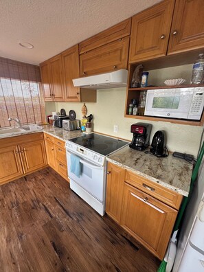 Une cuisine avec des meubles de rangement en bois, une cuisinière blanche, un four à micro-ondes et une machine à café.