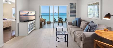 A modern living room with a television, a ceiling fan, a sofa, a coffee table, and a view of the ocean through large glass doors.