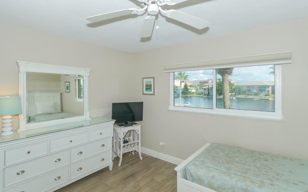 A bedroom with a large mirror, a TV on a small table, a bed, and a window with a view of a body of water.
