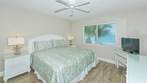 A bedroom with a bed, nightstands, a ceiling fan, a TV, and a window with blinds. - Endless Gulf Views, Endless Relaxation (Siesta Key)