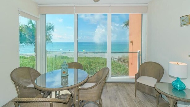 A room with a glass table and chairs, a ceiling fan, and a view of the beach and ocean. - Endless Gulf Views, Endless Relaxation (Siesta Key)