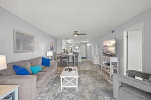 A living room with a grey sofa, a coffee table, and a TV on a stand. - Escape to the Gulf – Prime Beachfront Location (Siesta Key)