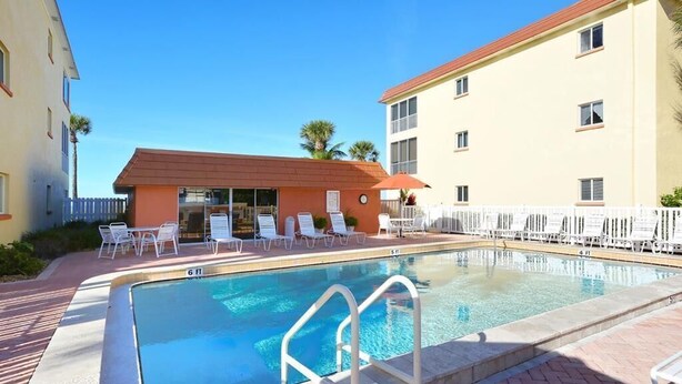 A swimming pool with lounge chairs and a small building with a red roof. - Escape to the Gulf – Prime Beachfront Location (Siesta Key)