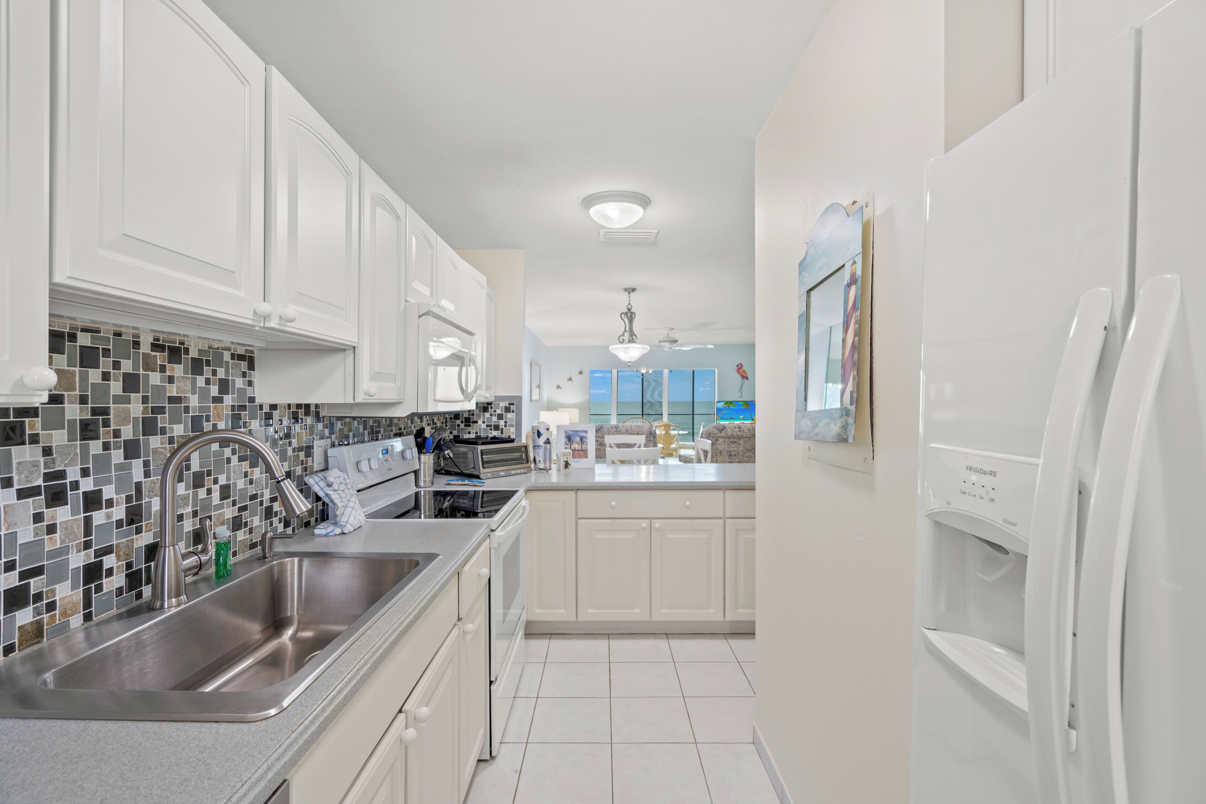 A modern kitchen with white cabinets, a stainless steel sink, and a tiled backsplash.