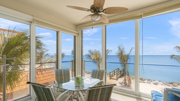 A room with a glass table and chairs, a ceiling fan, and a view of the beach. - Watch the Sunset from Your Gulf-Front Balcony (Siesta Key)