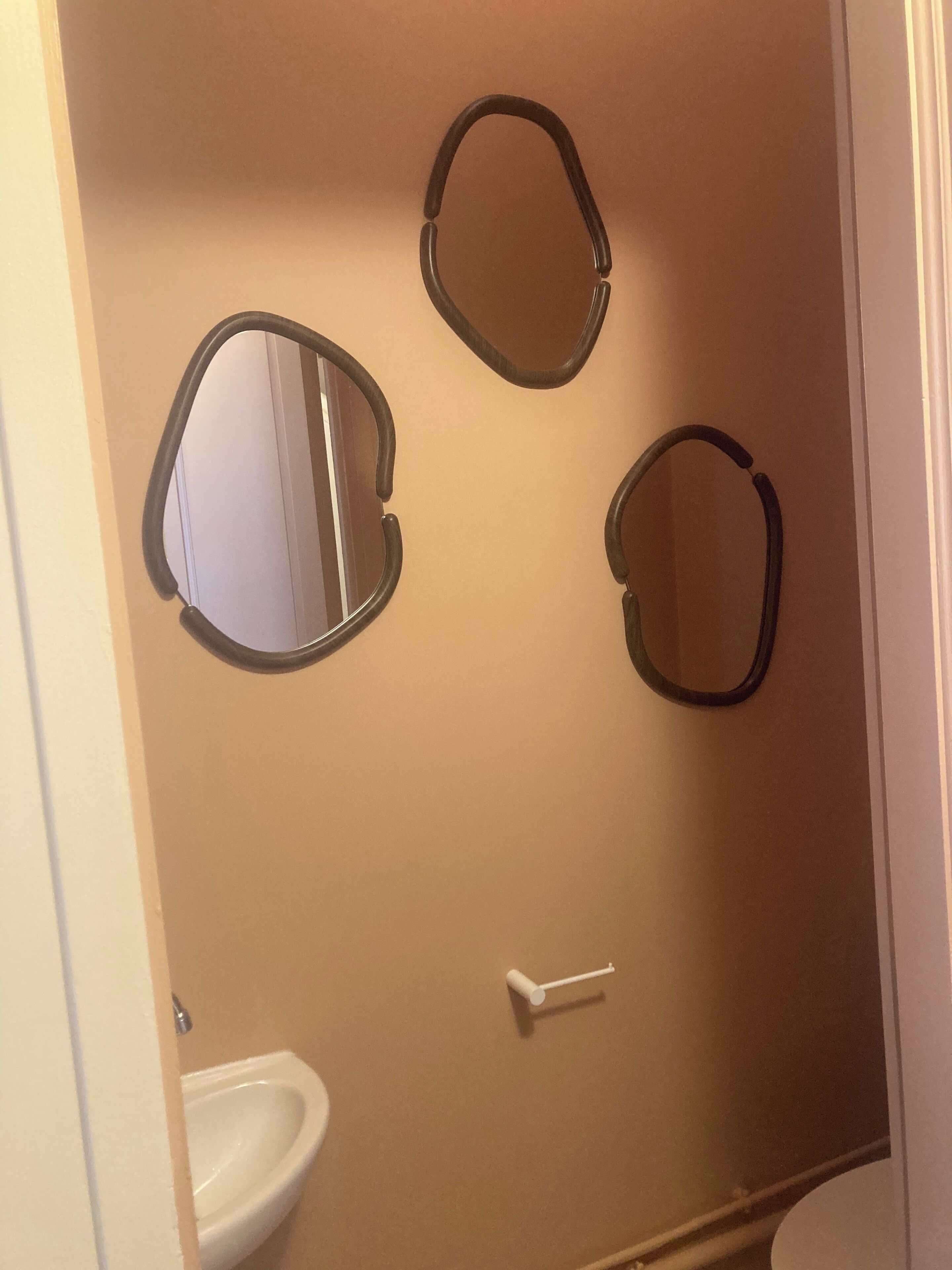 A bathroom with three oval mirrors on the wall, a white sink, and a toilet.