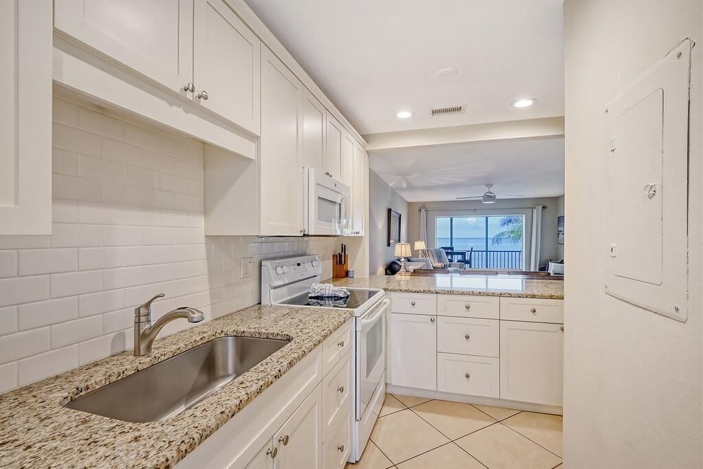 A modern kitchen with white cabinets, granite countertops, stainless steel sink, and a microwave.
