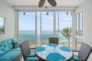 Ein Zimmer mit Blick auf den Strand, einem runden Glastisch, Korbstühlen und einem türkisfarbenen Sofa.