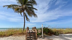 Una escalera de madera que da a una playa con una palmera y un cartel.