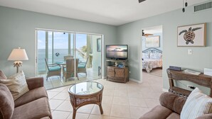 Una sala de estar con televisor, muebles de mimbre, una mesa de vidrio y vista al océano.
