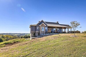 A house with a stone facade, a covered porch, and a view of the countryside.