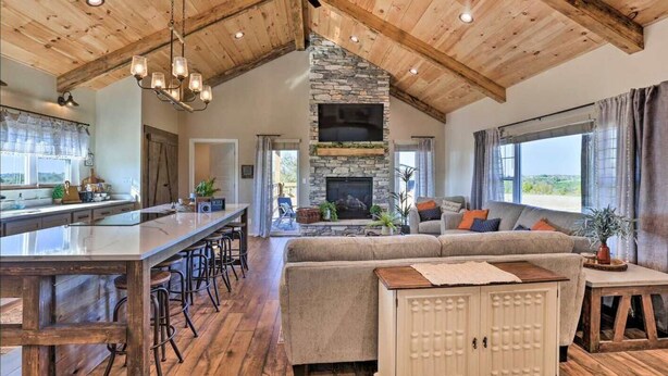 A spacious living area with a stone fireplace, a large wooden ceiling, and a bar area with stools. - Pool | Hot Tub | Pickleball | Firepit (Williamstown)