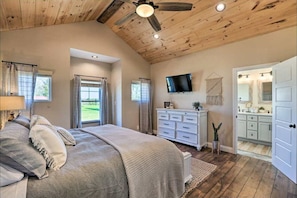 A bedroom with a bed, a dresser, a TV, and a bathroom with a sink and mirror. - Pool | Hot Tub | Pickleball | Firepit (Williamstown)