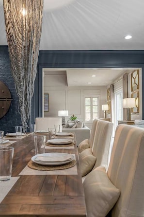 A dining area with a wooden table set for four, a chandelier, and a modern interior design with a blue accent wall and a sofa.