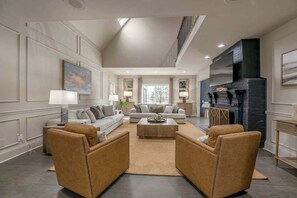 A spacious living room with a high ceiling, a fireplace, and a large window.