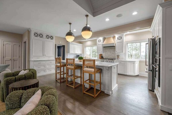 A spacious kitchen with white cabinetry, a central island with bar stools, and a dining area with a green upholstered sofa.