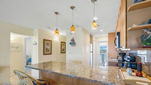 A kitchen with a granite countertop, hanging pendant lights, and a built-in stove. - Sun, Sand & Gulf-Front Views (Sarasota)
