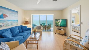 A living room with a blue sofa, a coffee table, a TV, and a balcony with a view of the ocean. - Sun, Sand & Gulf-Front Views (Sarasota)