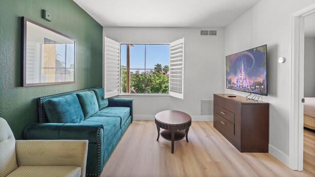 A room with a teal sofa, a round wooden table, a TV on a wooden cabinet, and a window with white shutters. - Orlando Comfort Close to Top Universal's Attractions (Orlando)