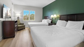 A hotel room with two beds, a dresser, a chair, a desk with lamps, and a window with blinds. - Orlando Comfort Close to Top Universal's Attractions (Orlando)