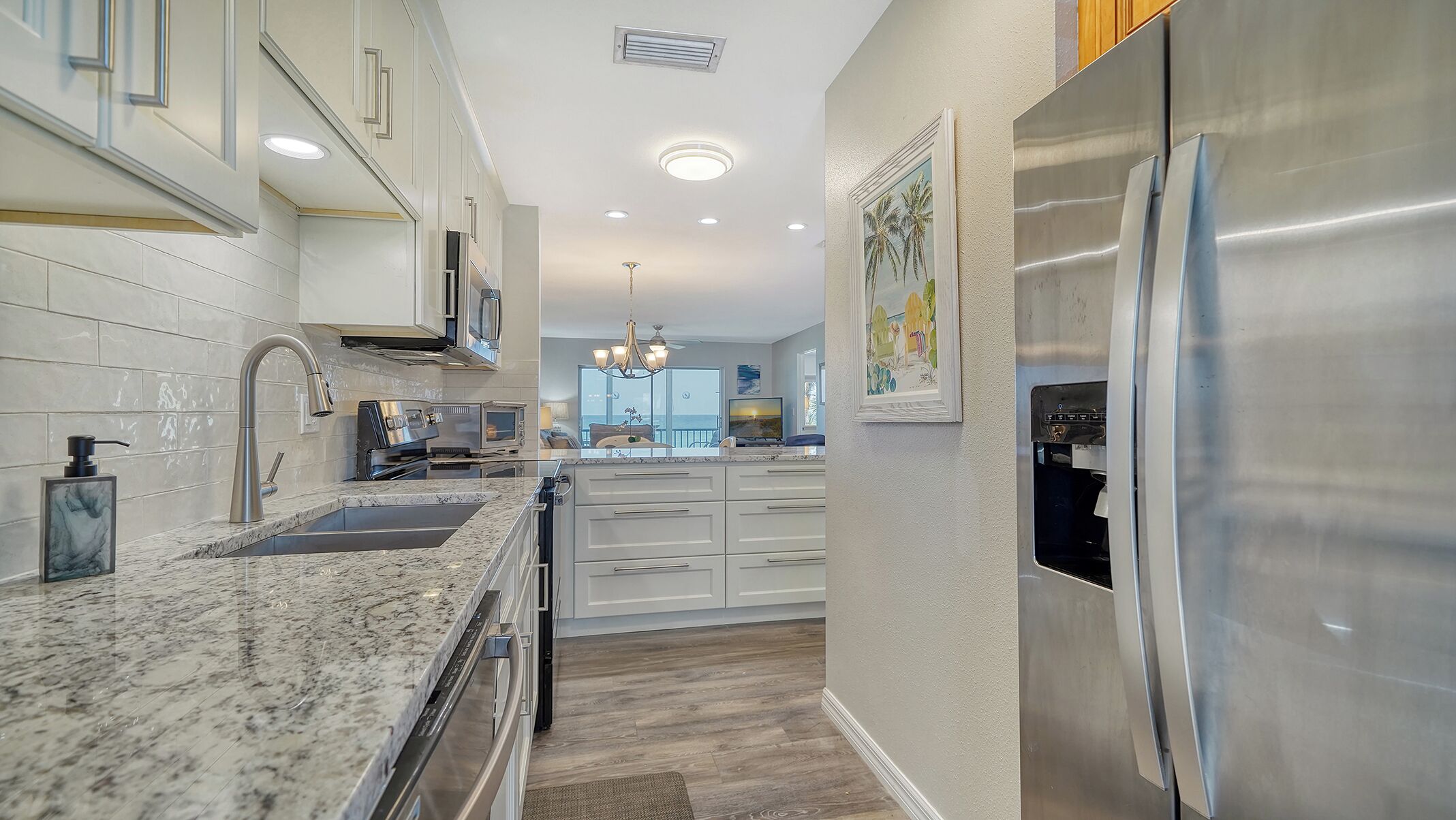 A modern kitchen with stainless steel appliances, white cabinetry, and a marble countertop.