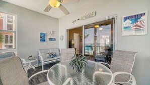 Ein Zimmer mit Glastisch, Korbstühlen, Deckenventilator und einem Poster zum Strandthema.