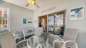 Ein Zimmer mit Glastisch, Korbstühlen, Deckenventilator und einem Poster zum Strandthema.