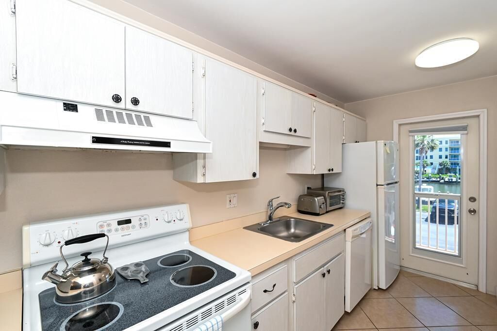 A kitchen with white cabinets, a stove, a sink, and a refrigerator.