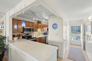 A modern kitchen with wooden cabinets, a central island, pendant lights, and a view of the outside through a door. - Gulf-Front Vacation Done Right (Sarasota)