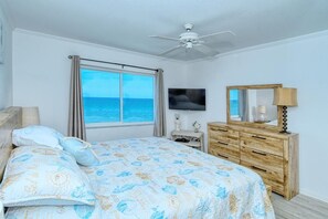 Une chambre à coucher avec un lit, une commode en bois, un téléviseur et une fenêtre donnant sur l’océan.