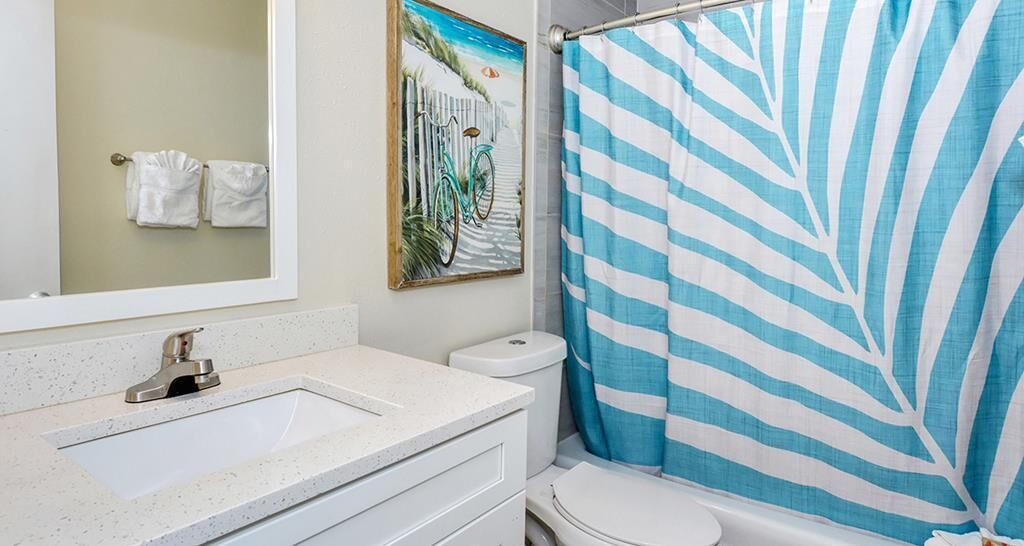 A bathroom with a white sink, a toilet, and a shower curtain with a leaf pattern.